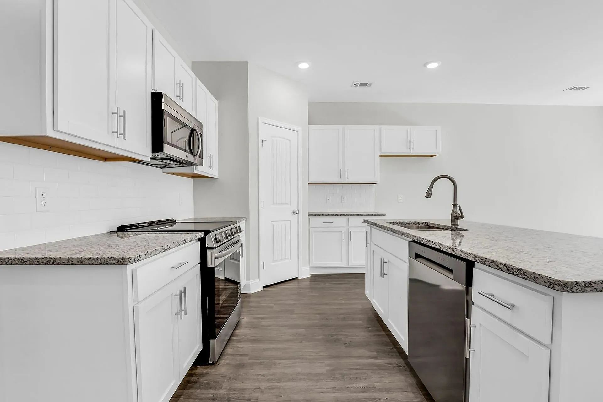 Townhomes with Attached Garages in Statesboro, GA - The Outpost - Modern Kitchen With White Cabinets, Granite Countertops, Stainless Steel Appliances, Island Sink, And Wood-Style Flooring.