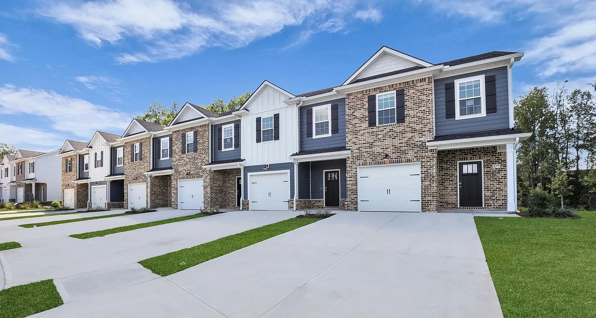 Dog-Friendly Townhomes in Statesboro, GA - The Outpost - Modern Townhome Exterior With Brick Facades, Attached Garages, Wide Driveways, Green Lawns, And Blue Sky.