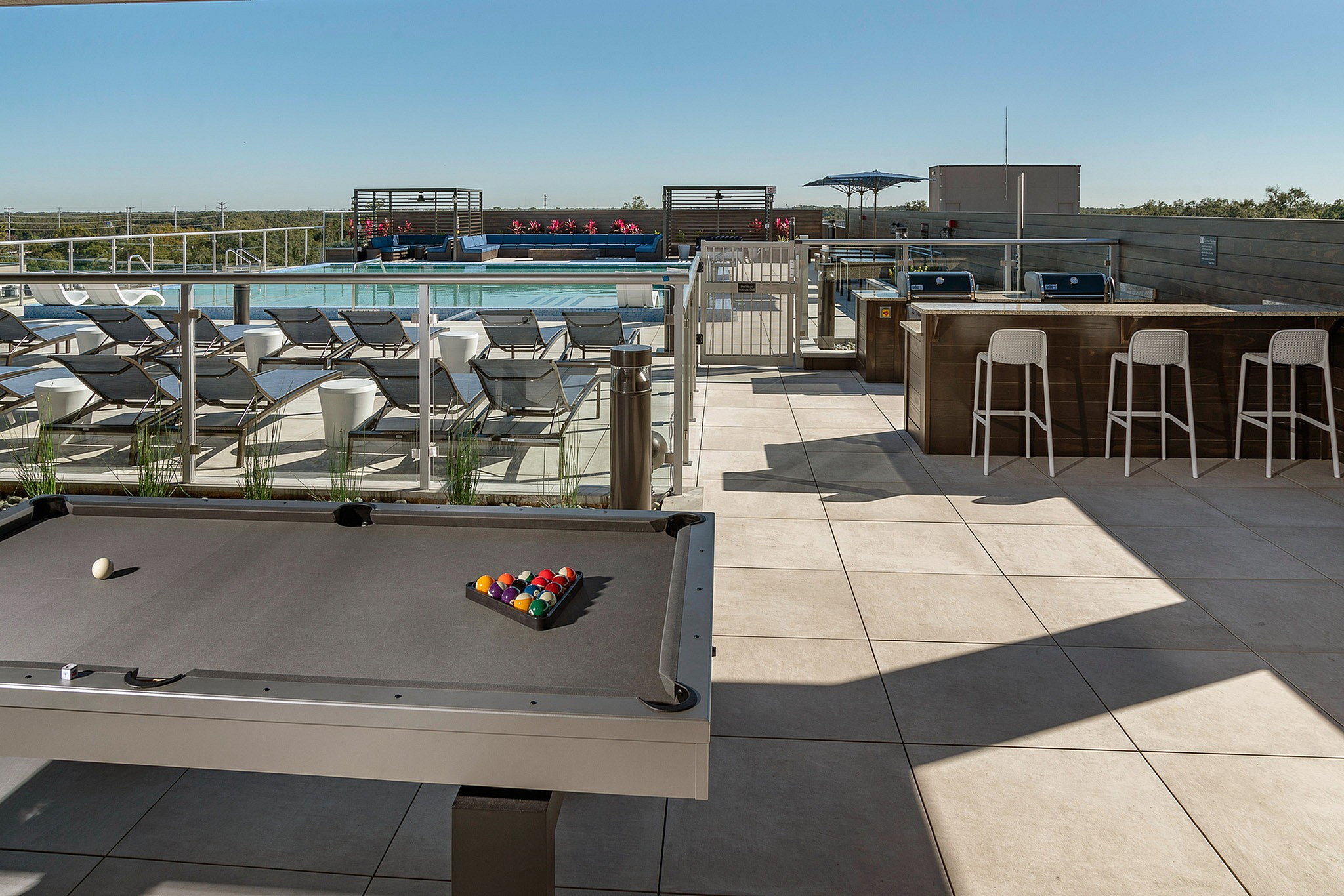 Luxurious rooftop terrace featuring a sparkling pool, stylish lounge chairs, pool table, and elegant bar seating with scenic views.