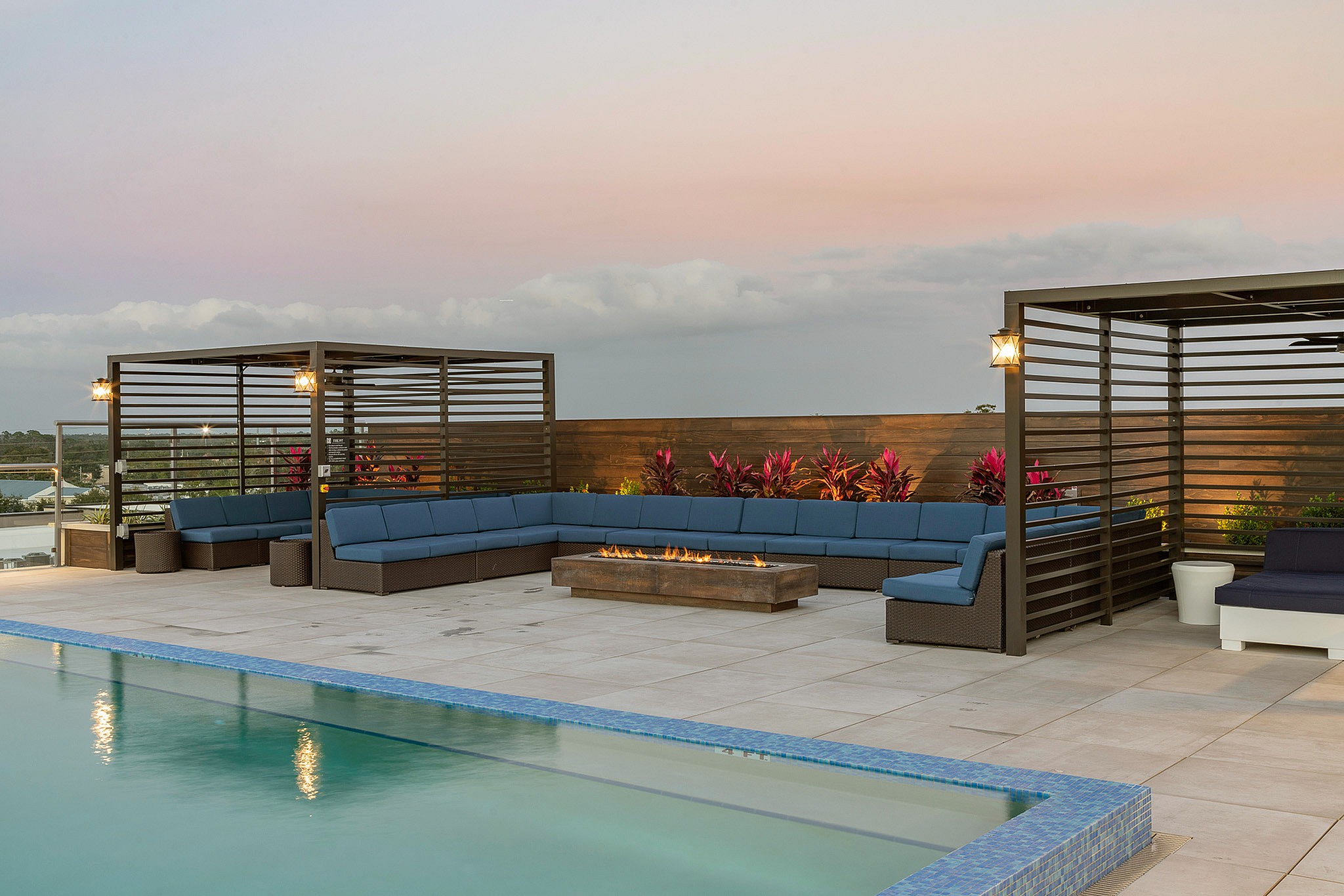 Elegant rooftop patio with modern cabanas, a cozy fire pit, and a refreshing pool set against a serene sunset sky.