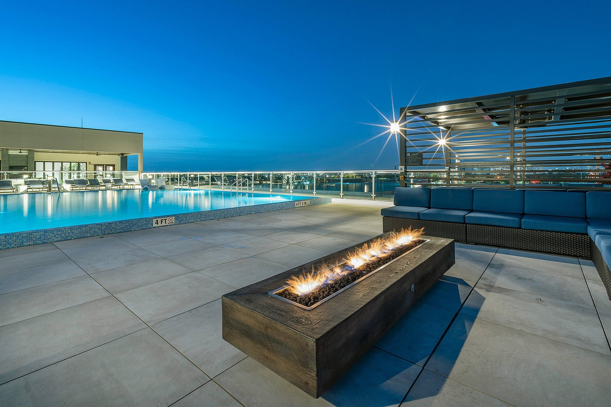 Luxurious outdoor rooftop terrace with a sparkling pool, cozy fire pit, and modern seating, perfect for relaxation and entertaining.
