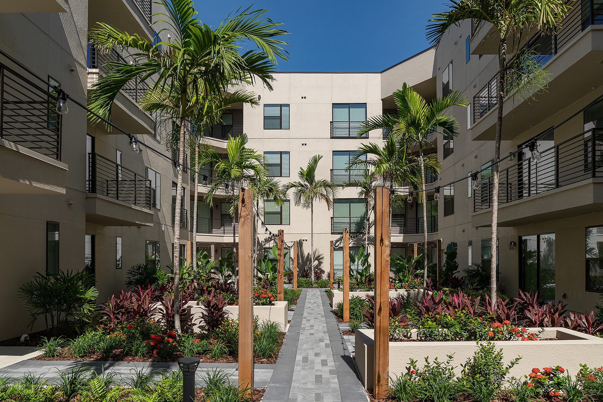 Modern apartment courtyard with lush greenery, palm trees, and elegant walkway, creating a serene oasis for residents.