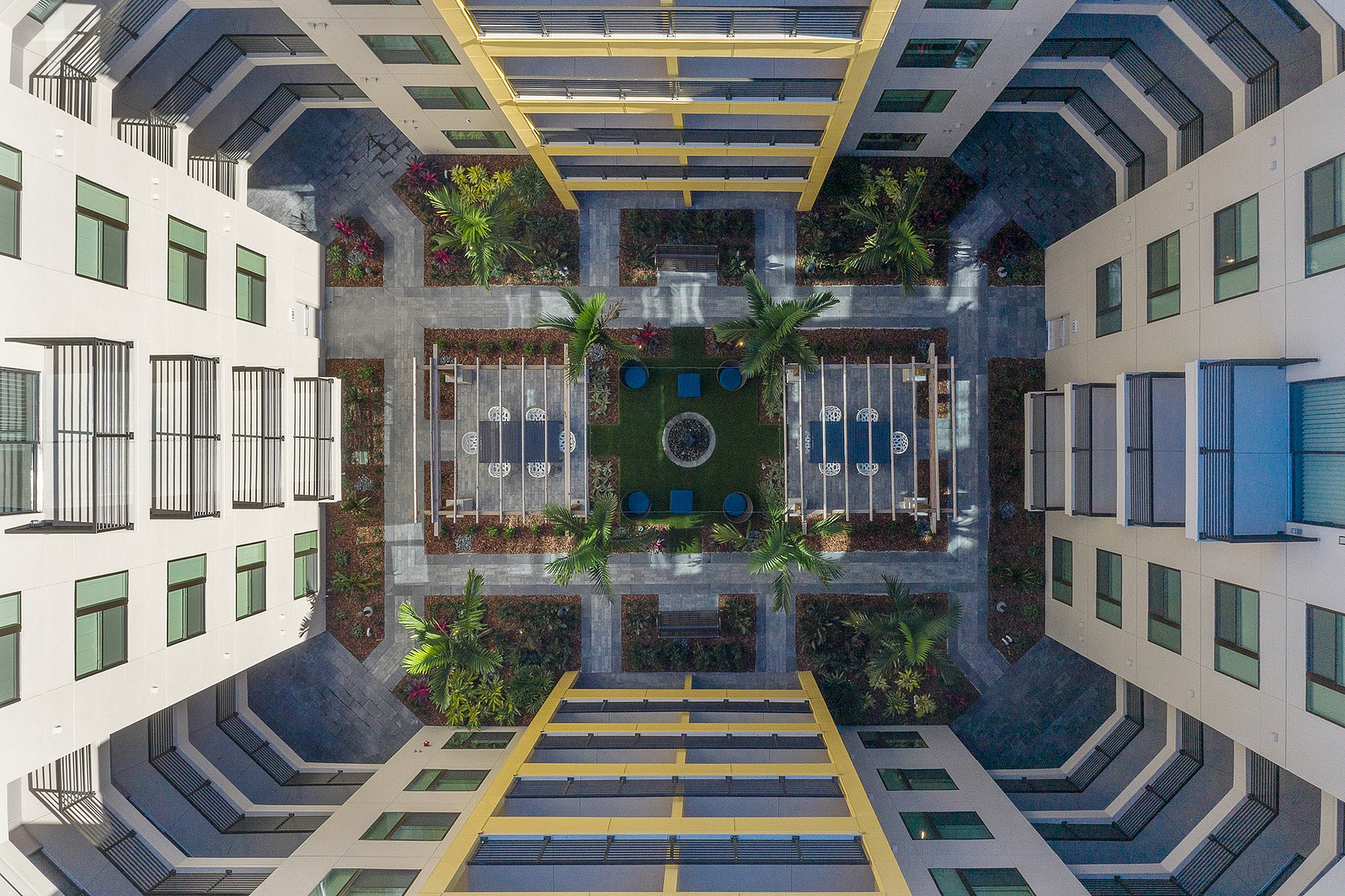 Aerial view of a beautifully landscaped apartment courtyard featuring lush greenery, symmetrical pathways, and inviting seating areas.