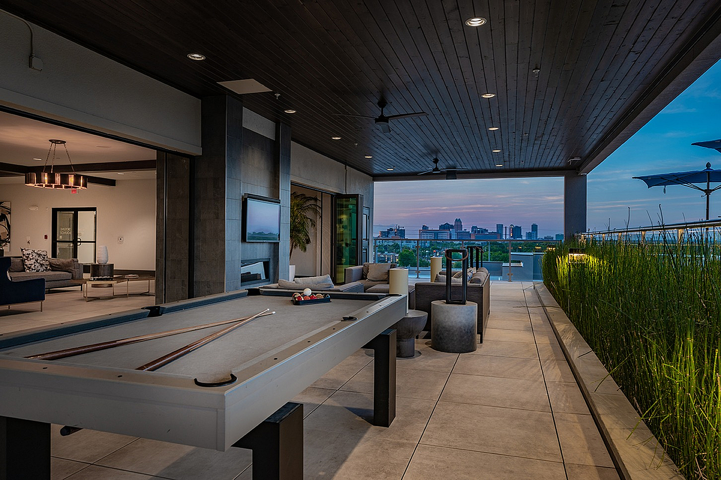 Luxurious rooftop patio with elegant lounge area, pool table, and stunning city skyline views at sunset.