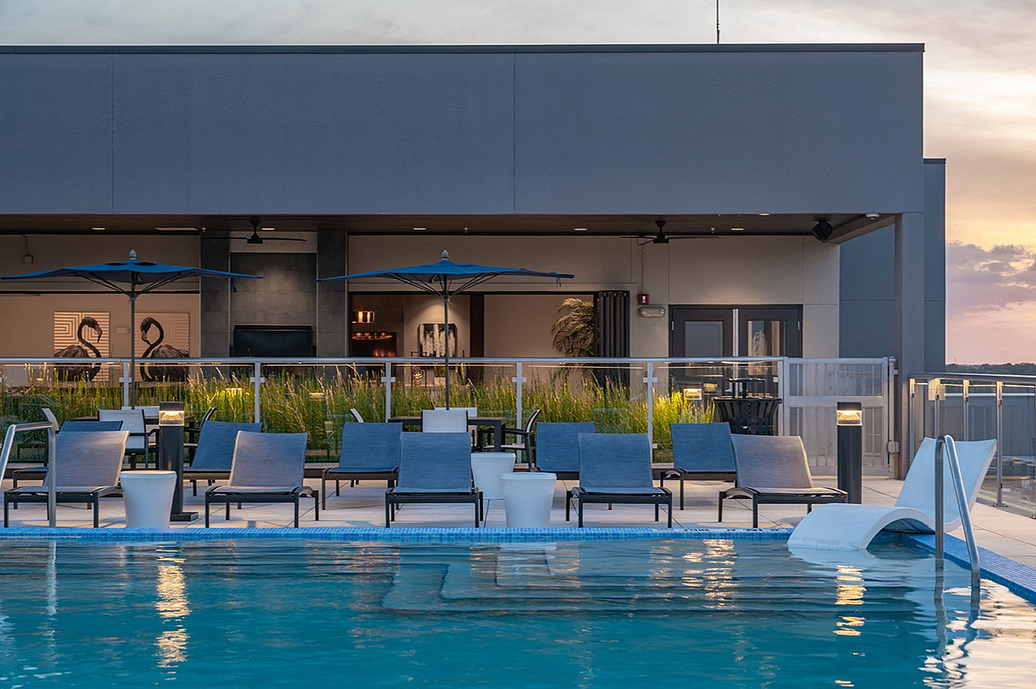 Chic rooftop pool area with modern lounge chairs and umbrella seating, offering a serene sunset view.