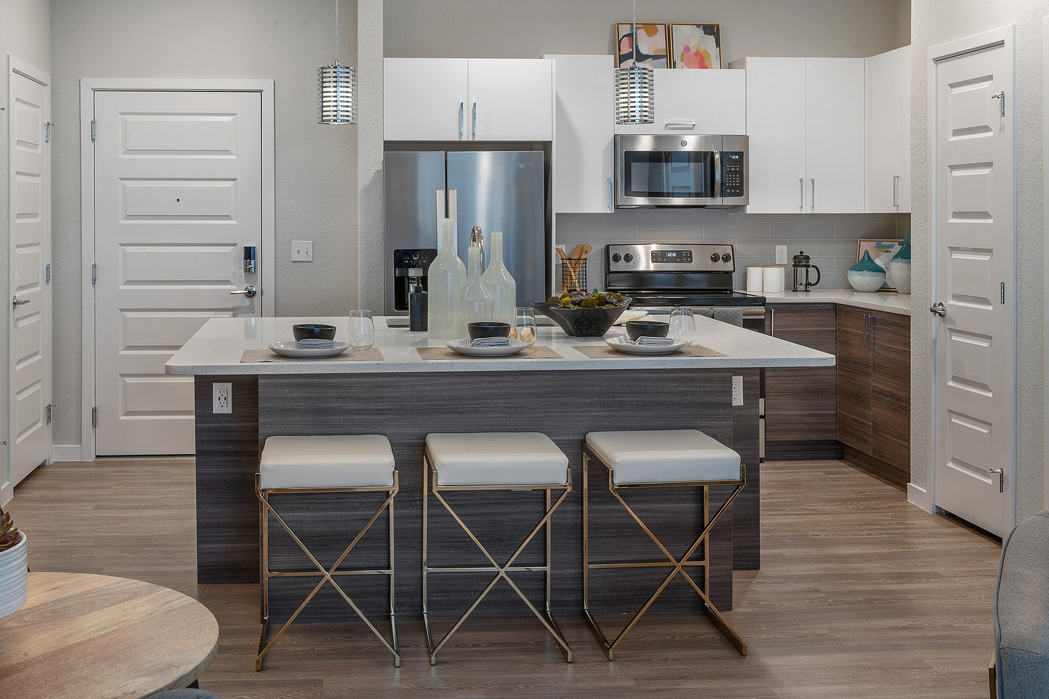 Modern kitchen with sleek stainless steel appliances, chic pendant lighting, and a stylish island with seating for three in a contemporary apartment.