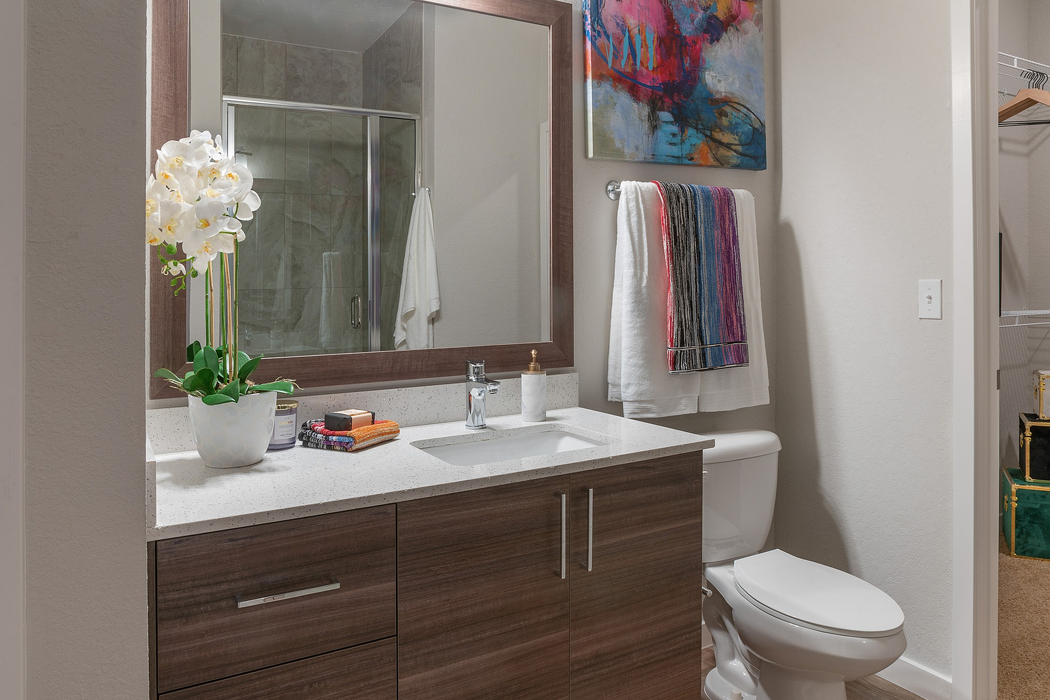 Elegant bathroom featuring modern wood cabinetry, sleek countertop, vibrant artwork, and a touch of nature with potted orchids.