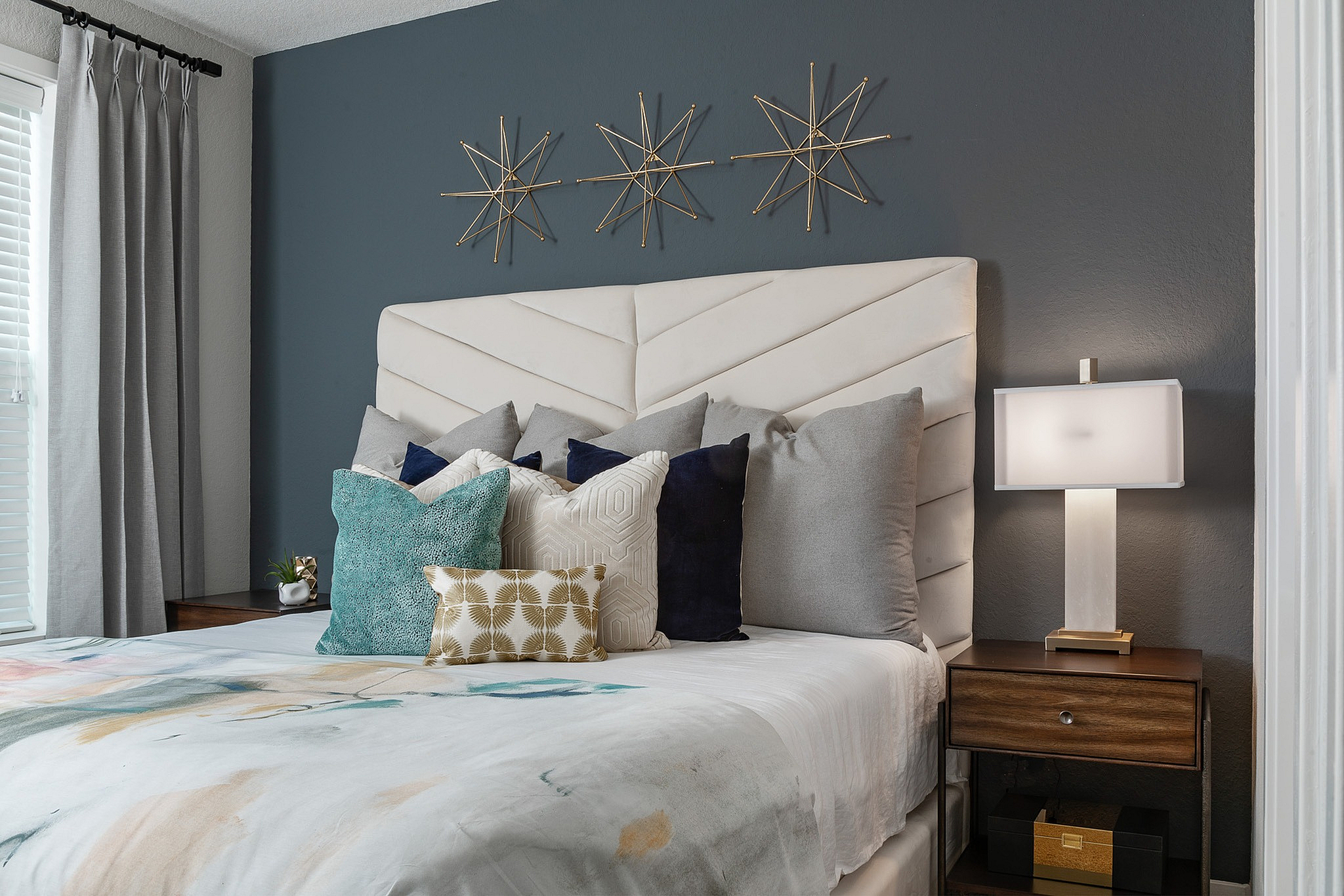 Elegant bedroom with modern decor, featuring a plush headboard, stylish pillows, and a sleek nightstand with a contemporary lamp.