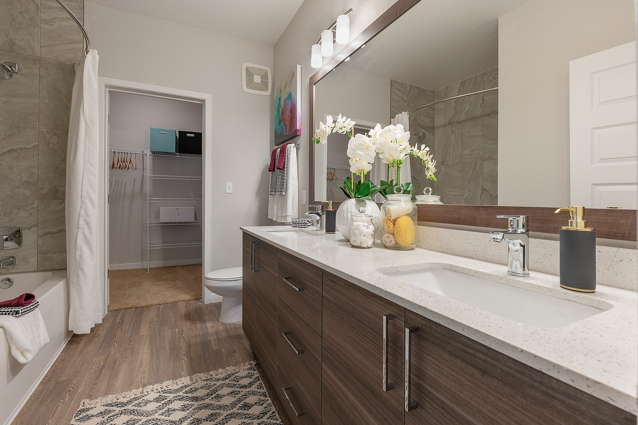 Modern bathroom with elegant vanity, dual sinks, decorative orchids, and a walk-in closet in stylish apartment.