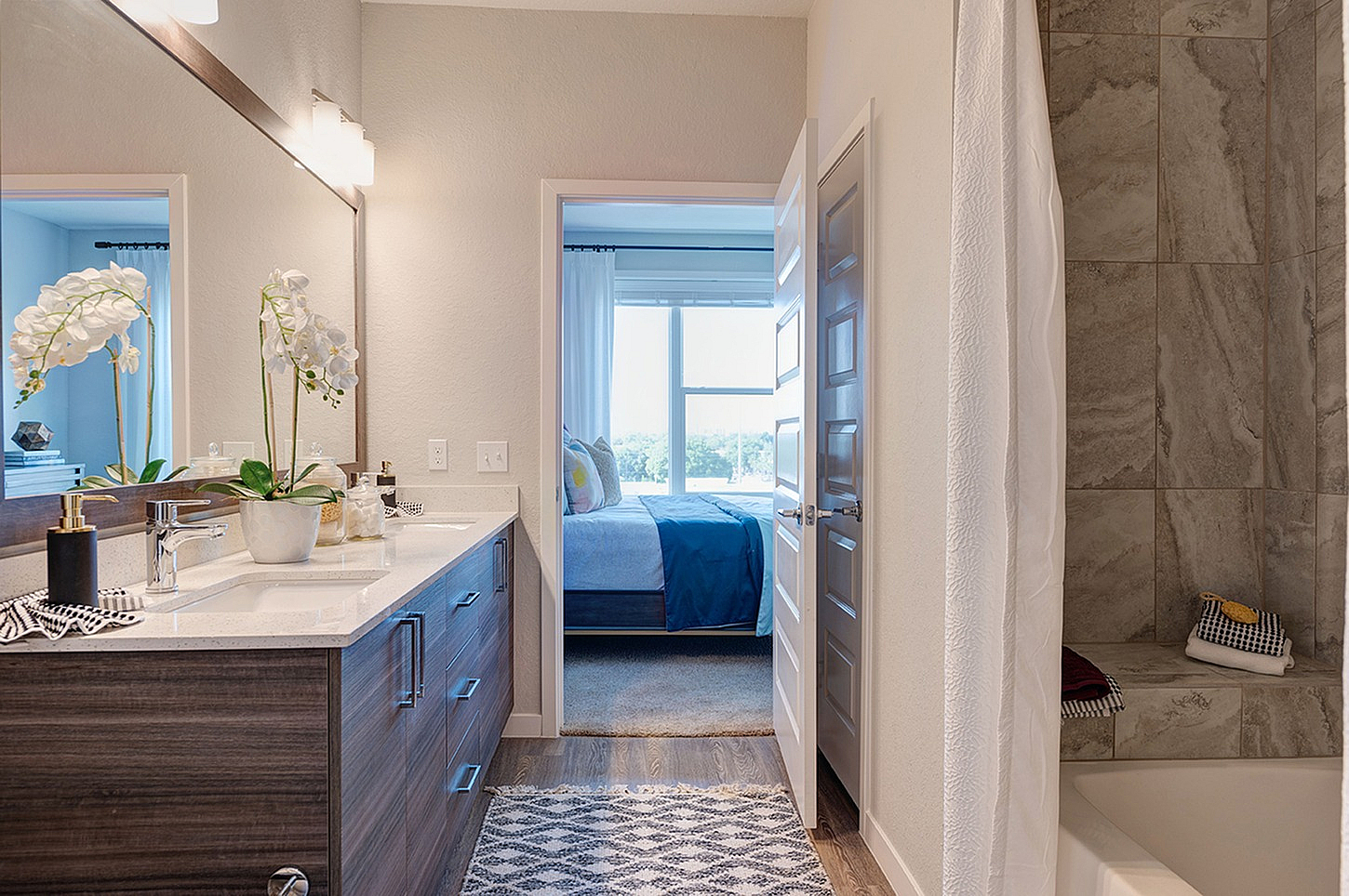 Elegant apartment bathroom with modern sink, stylish wooden cabinetry, decorative plants, and a view into a cozy bedroom with large window.