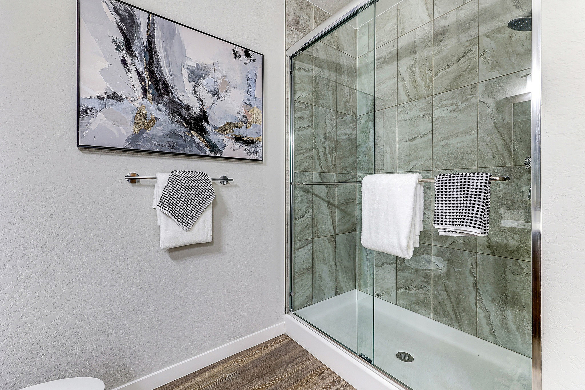 Elegant bathroom featuring a sleek, glass-enclosed shower with modern tile design, complemented by contemporary artwork and fresh towels for a luxurious touch.