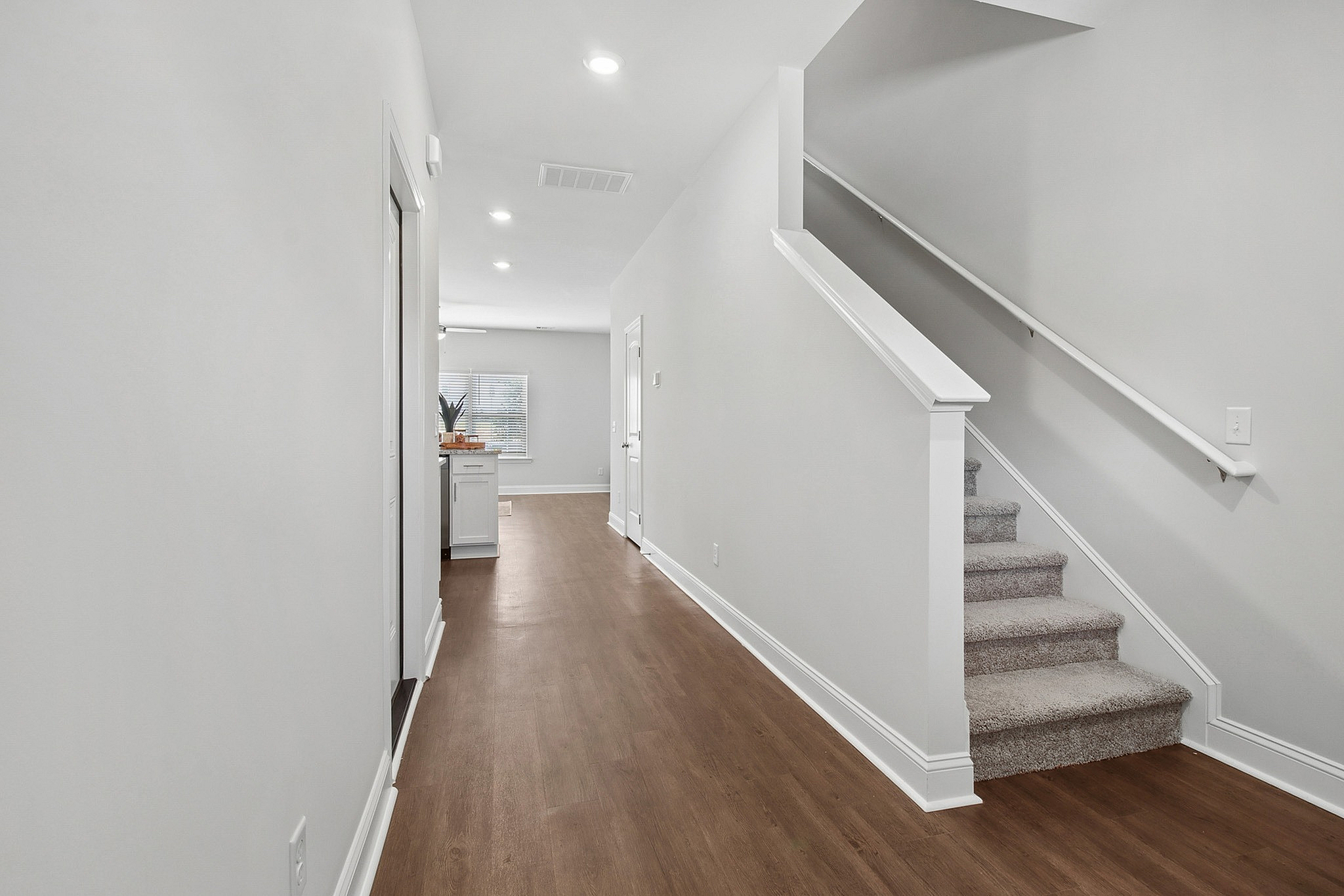 Bright and contemporary hallway with wooden flooring, leading to an inviting open space, complemented by a modern staircase.
