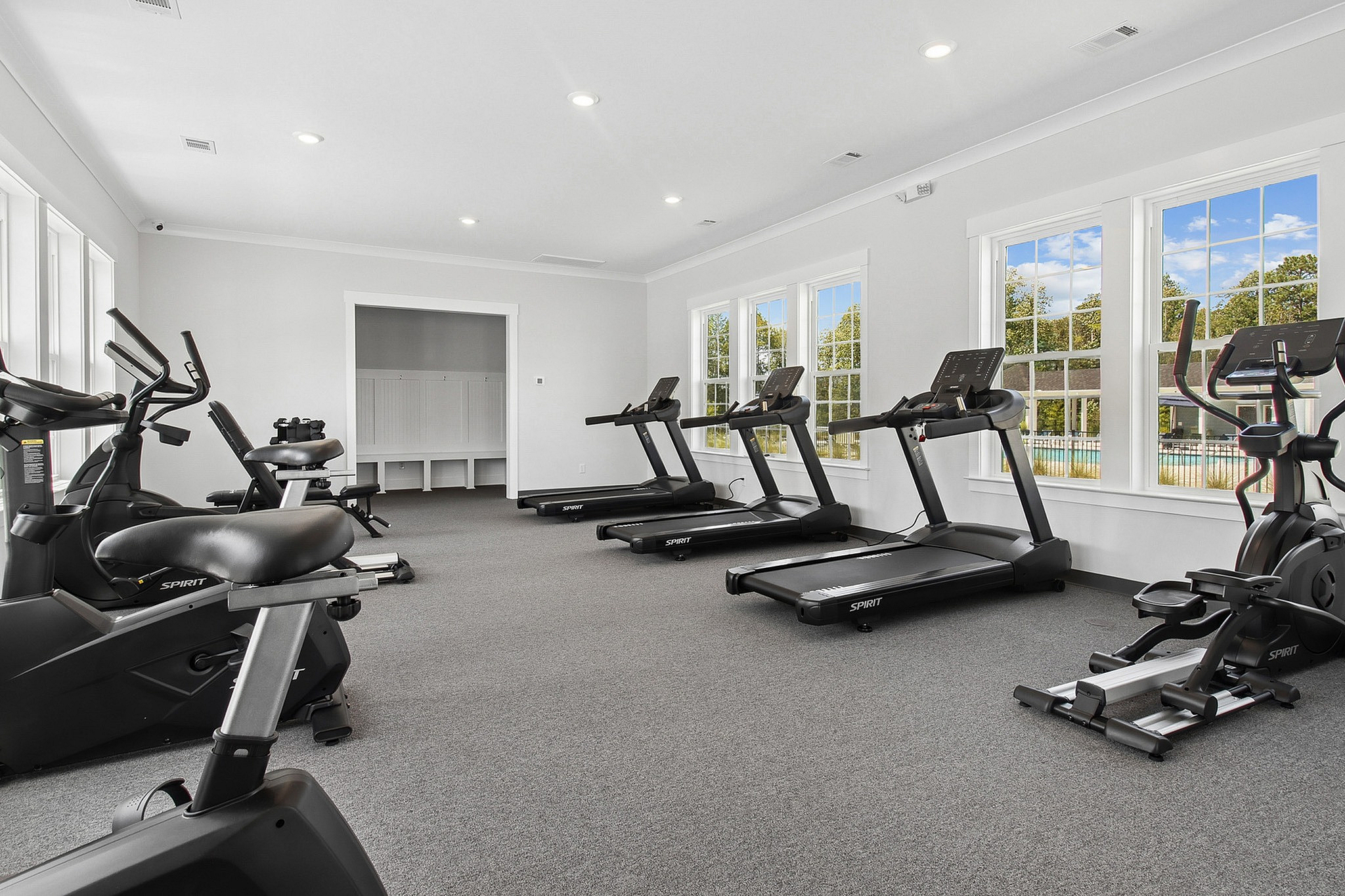 Bright and modern fitness center with large windows overlooking lush greenery, equipped with stationary bikes and treadmills.
