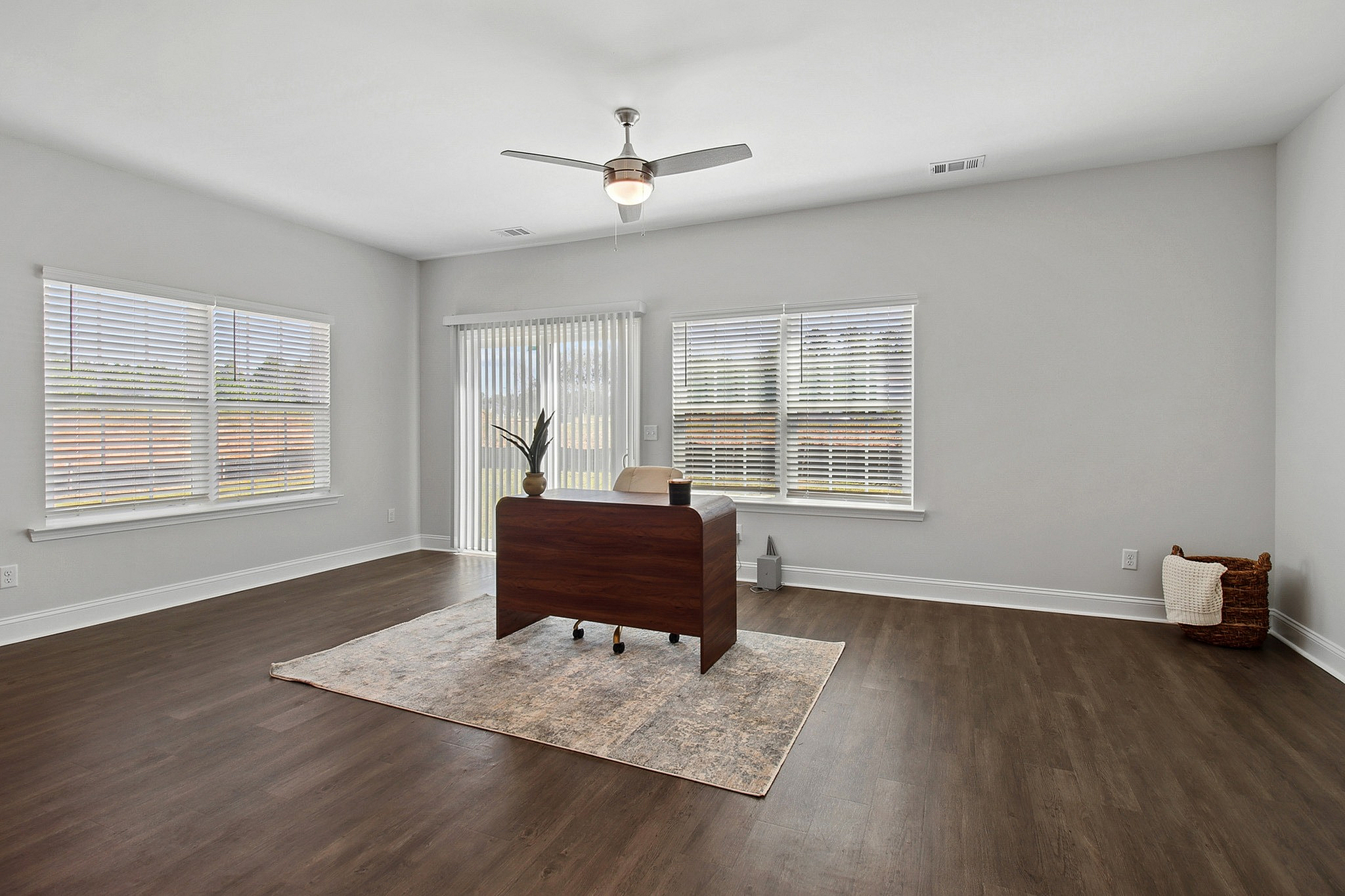 Elegant home office space with large windows, sleek wooden desk, and modern decor on polished wood flooring.