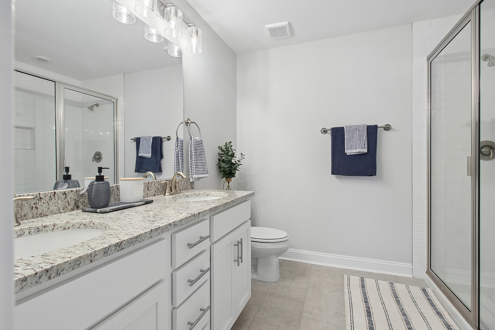Elegant bathroom featuring dual sinks with modern fixtures, granite countertop, glass shower, and chic lighting.