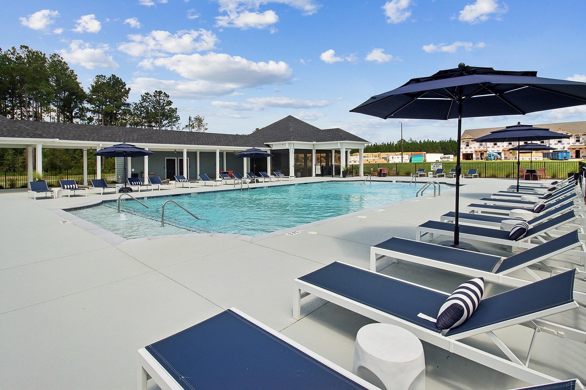 Luxurious outdoor swimming pool area with modern lounge chairs and stylish umbrellas, perfect for relaxation and leisure under the clear blue sky.