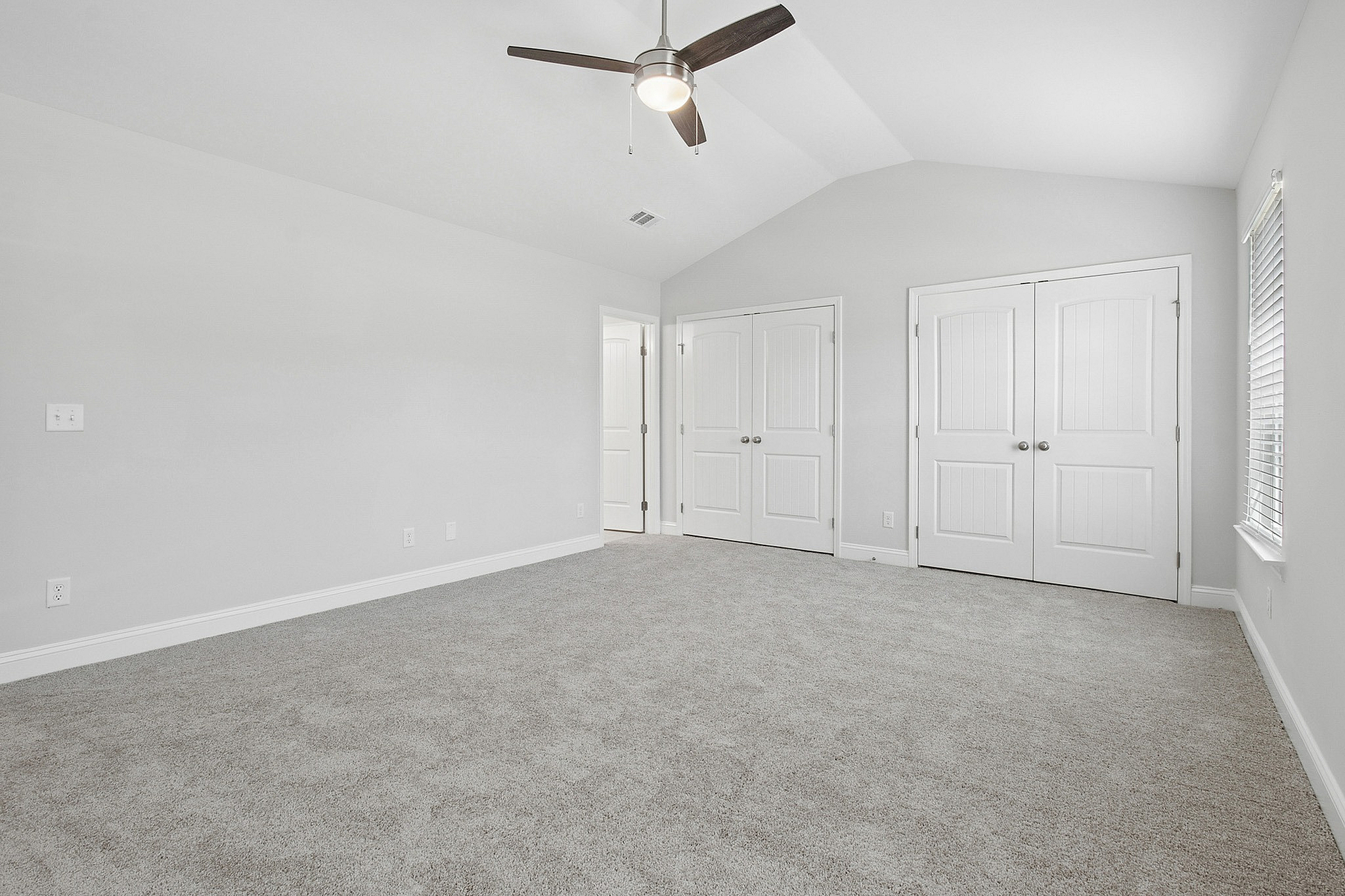 Bright and spacious bedroom with plush carpeting and modern fan, featuring double closets and ample natural light from large window.
