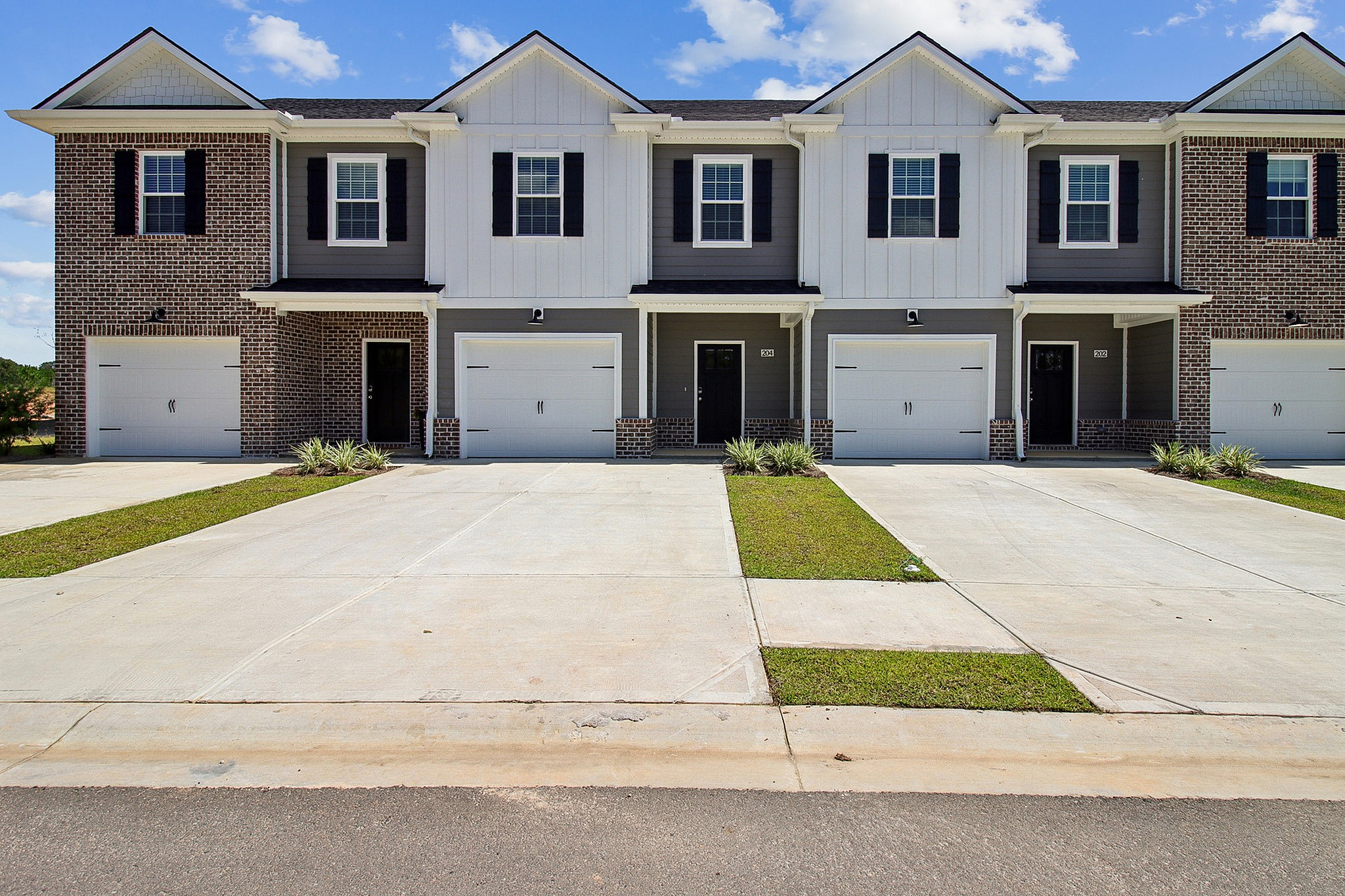 Charming townhomes with elegant brick and siding exterior, featuring driveways leading to spacious garages, set against a blue sky backdrop.
