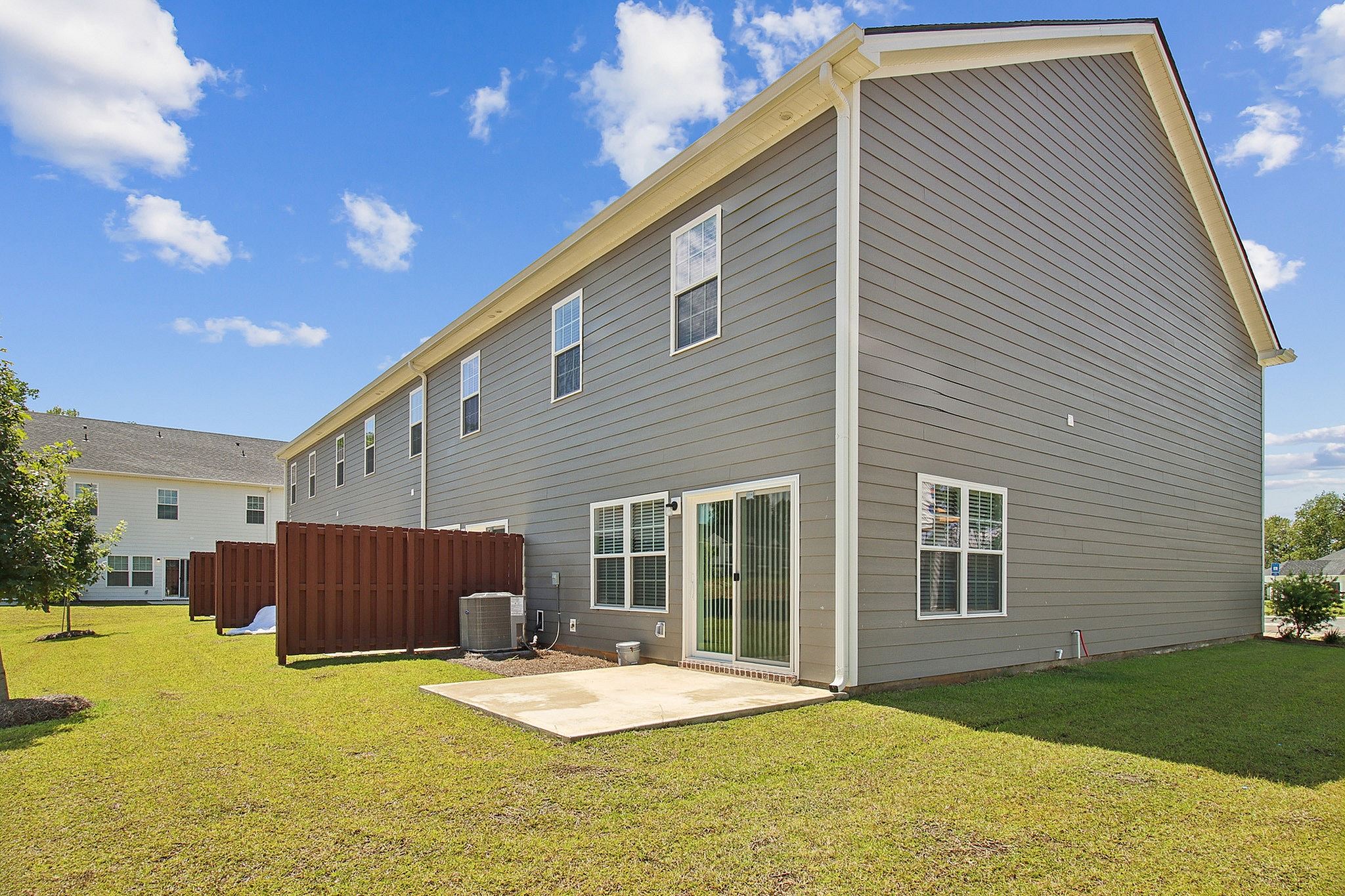 Charming townhouse exterior with modern siding and private fenced patio, surrounded by lush green lawn under a bright blue sky.