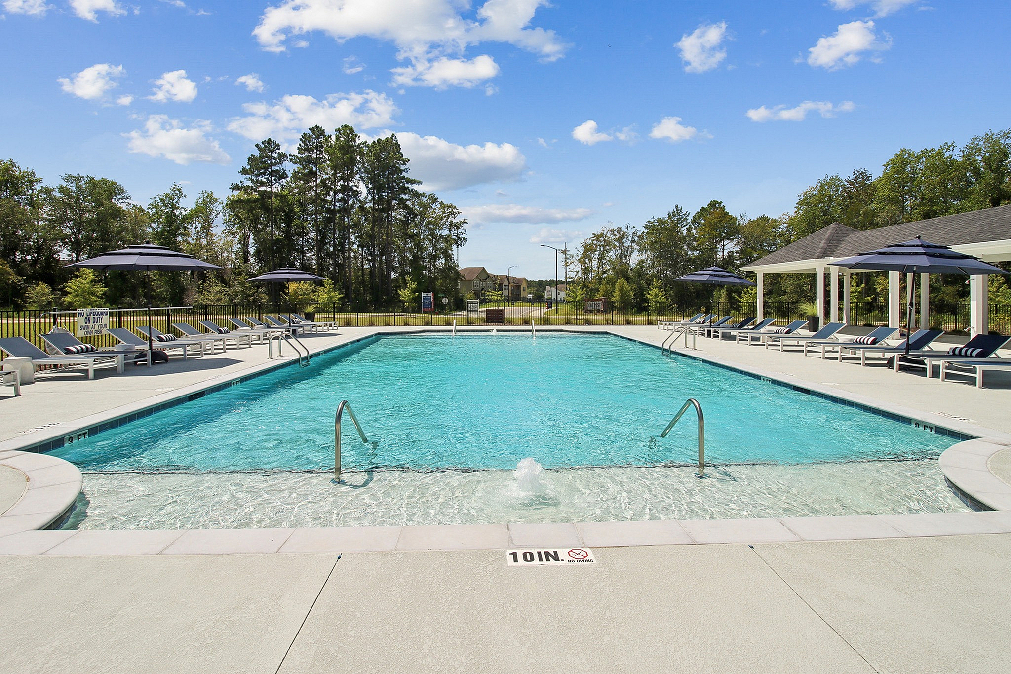 Inviting outdoor pool area with crystal-clear water, surrounded by stylish sun loungers and umbrellas, set against a backdrop of lush greenery and a bright, blue sky.
