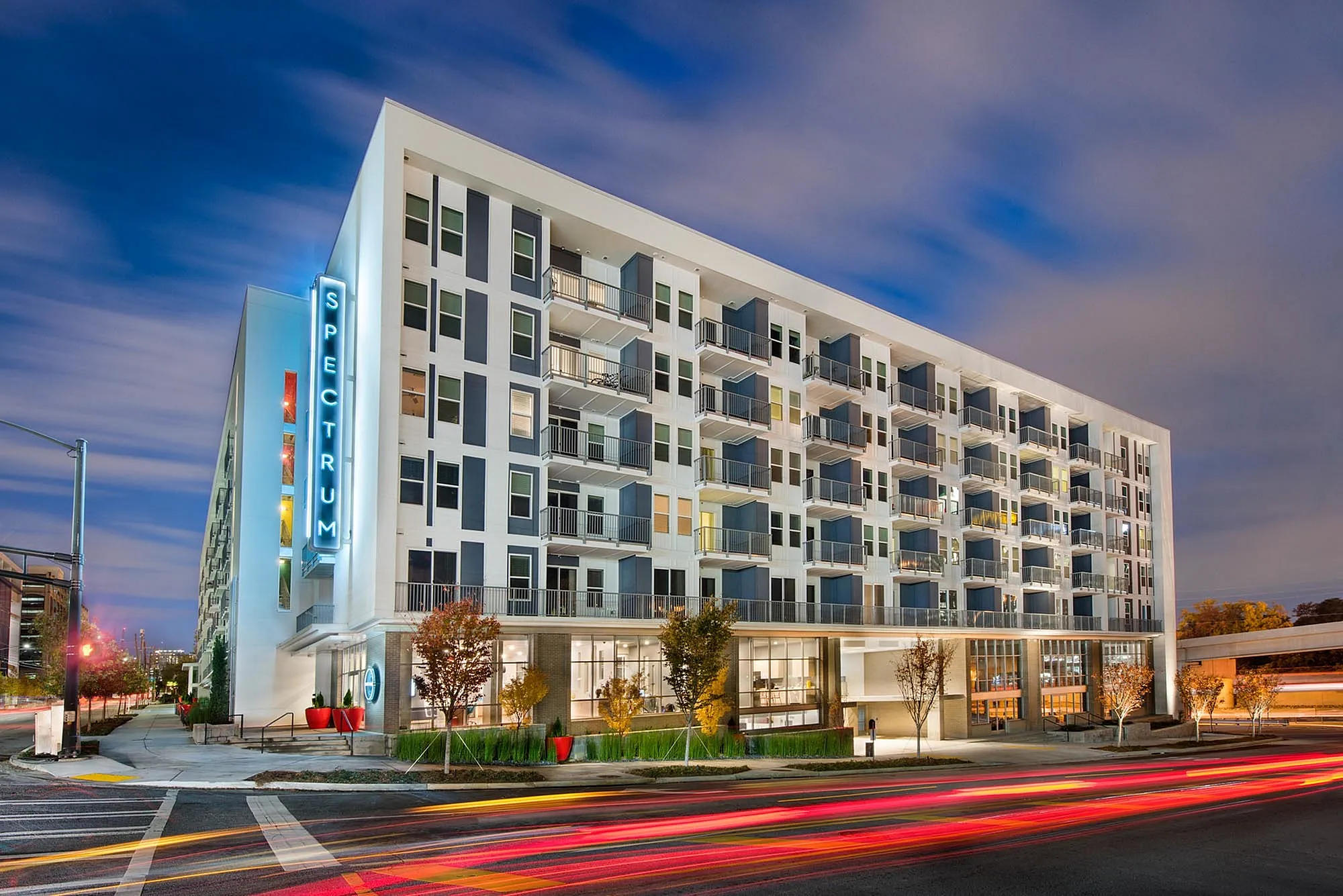 Stunning modern apartment building \'Spectrum\' illuminated at night with vibrant city lights and sleek architectural design.
