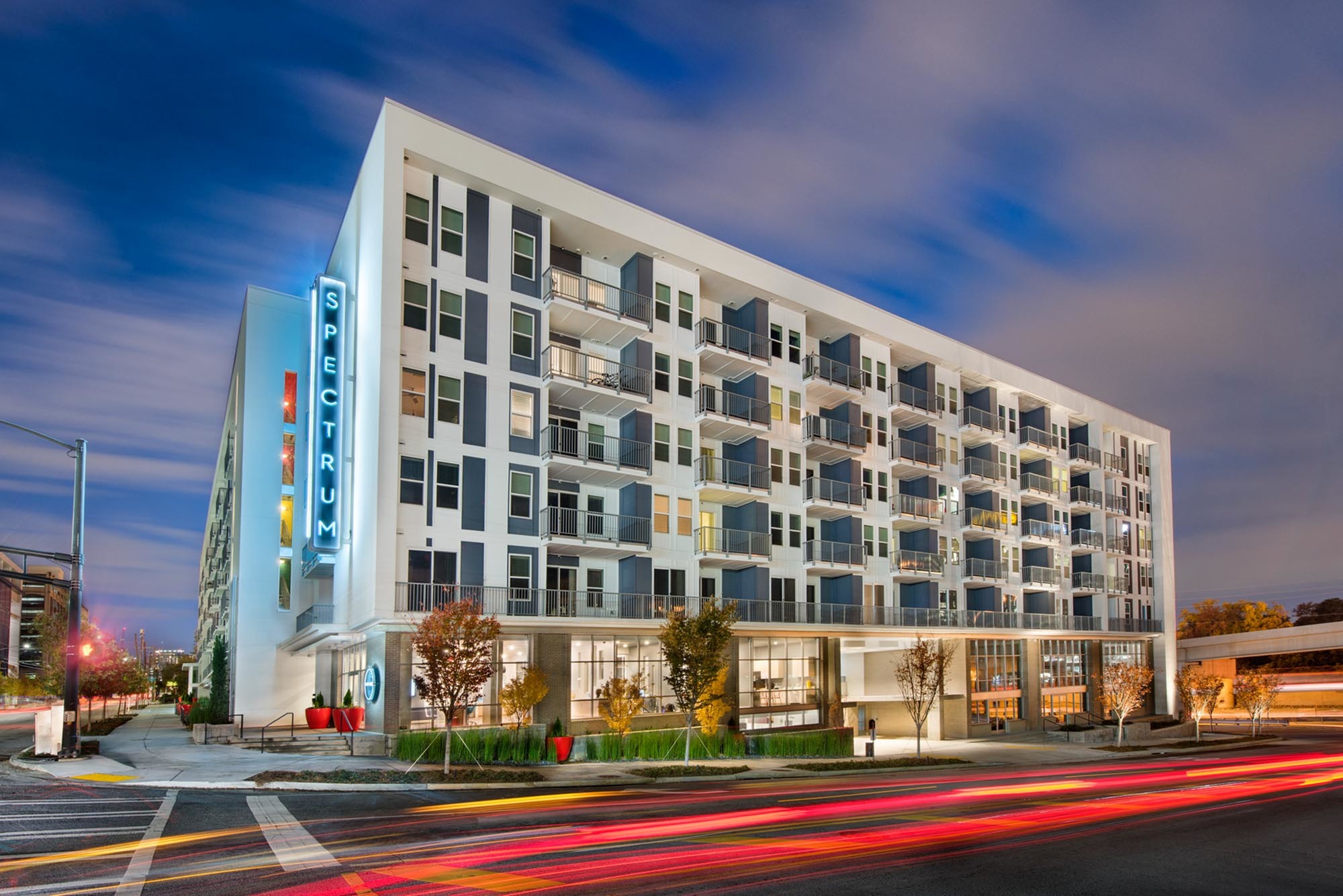 Modern apartment building with illuminated Spectrum sign, featuring multiple balconies and vibrant evening lighting.