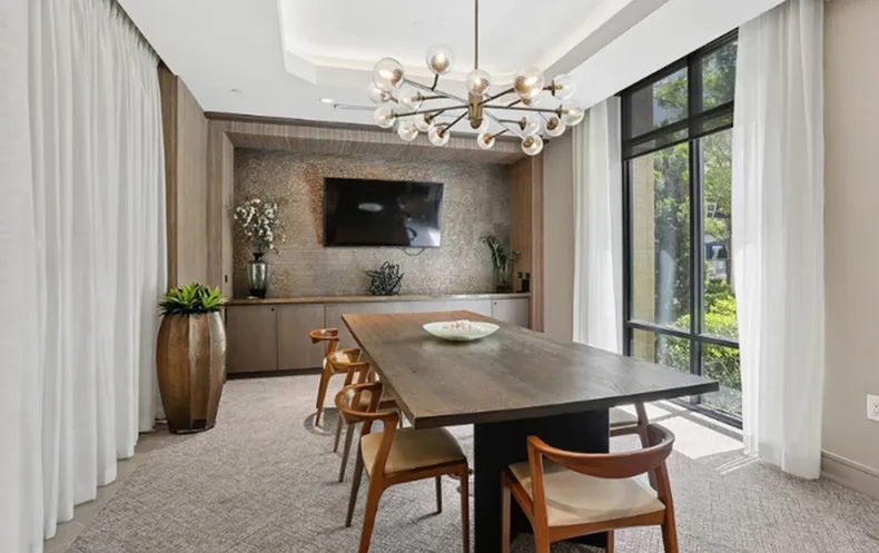 Elegant dining room with a modern chandelier, sleek wooden table, and large windows offering a scenic view.