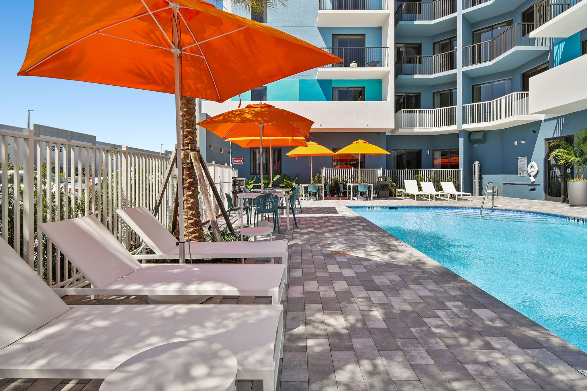 Vibrant apartment pool area featuring bright orange umbrellas, sleek lounge chairs, and crystal-clear water, offering a perfect relaxation spot.