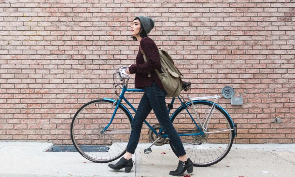 woman walking with bicycle against brick wall outside