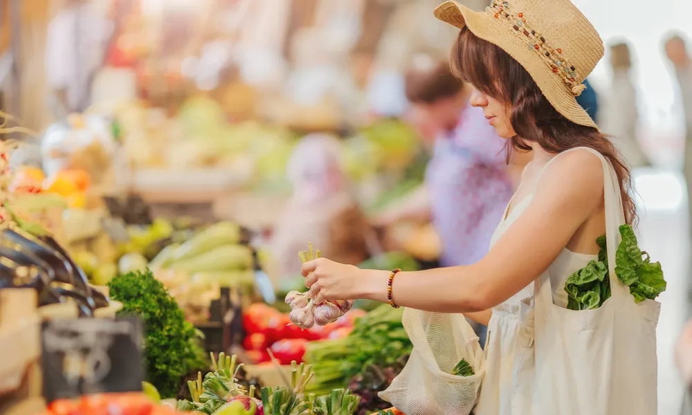 woman wearing big hat picking up garlic at farmers market