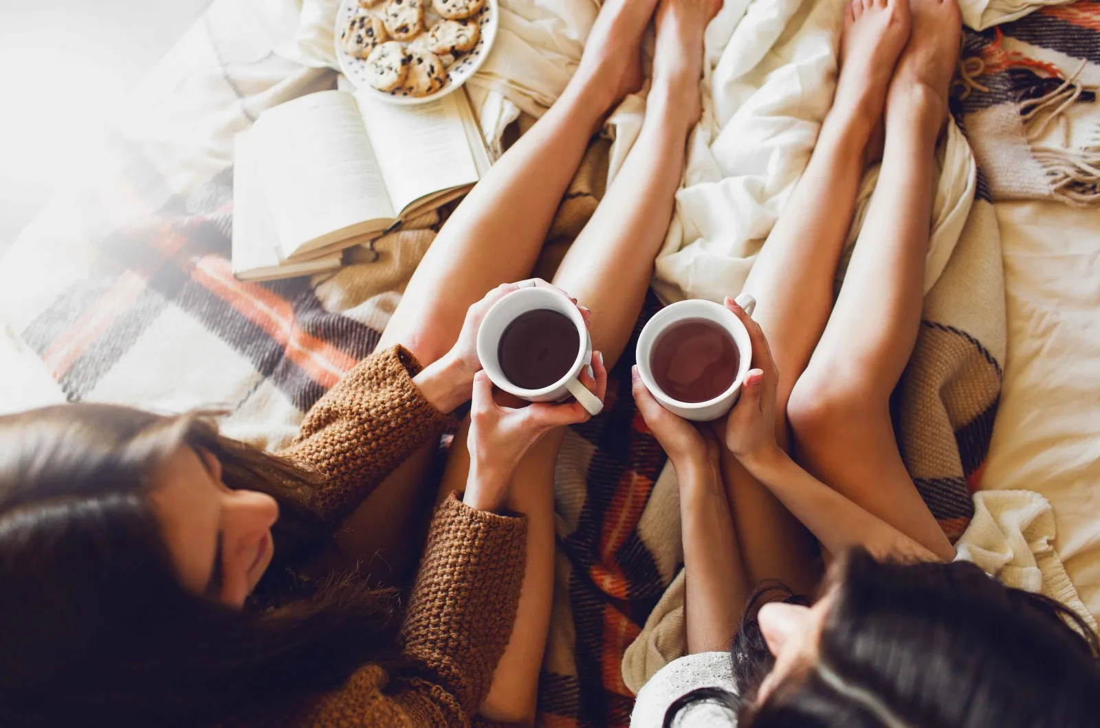 two girls with coffee sitting on bed