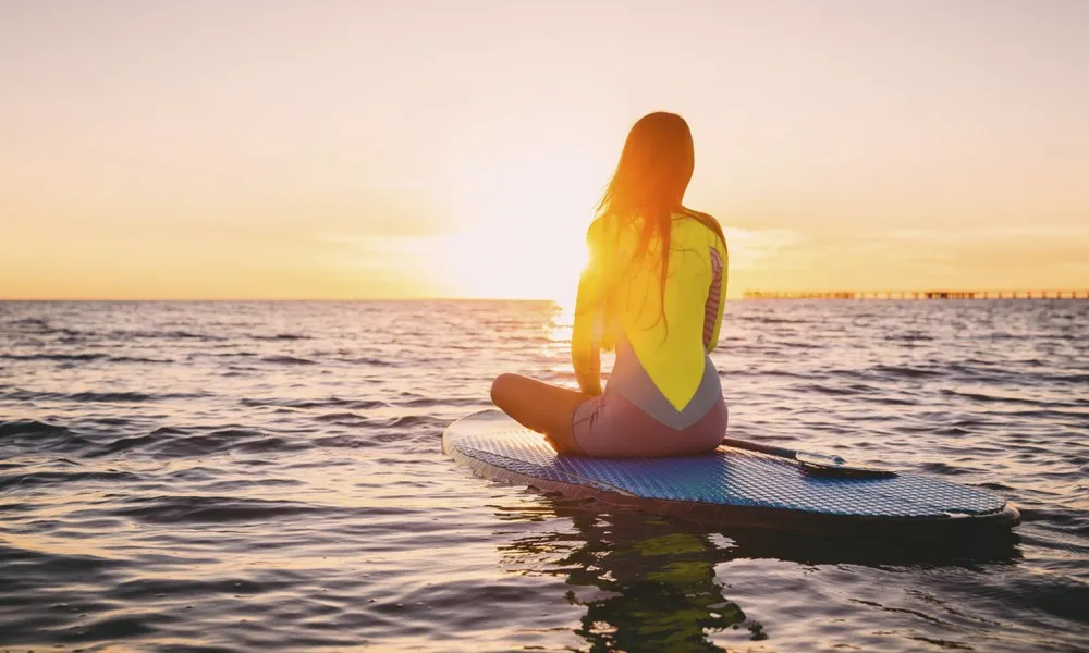 woman looking into sunset on a wake board in beach water