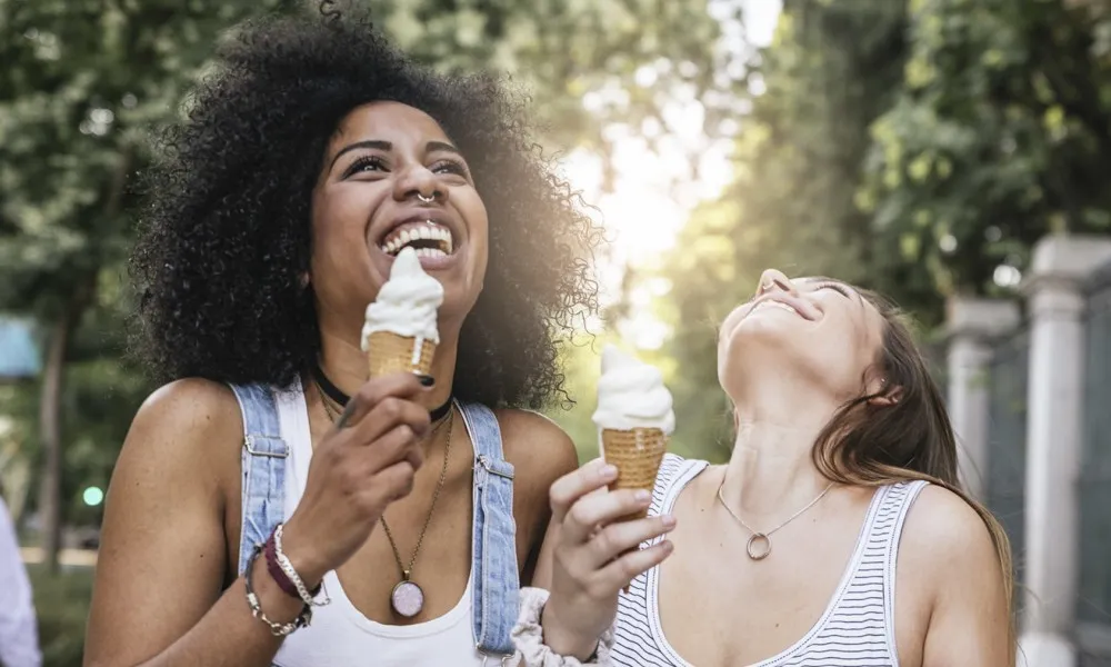 two laughing women with ice cream cones on sidewalk on sunny day