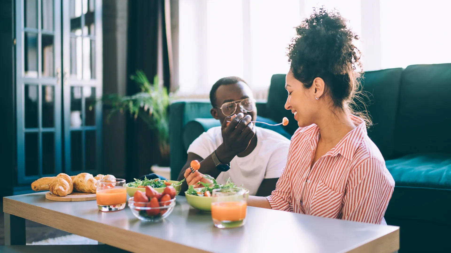 man feeding woman with food on coffee table in living area