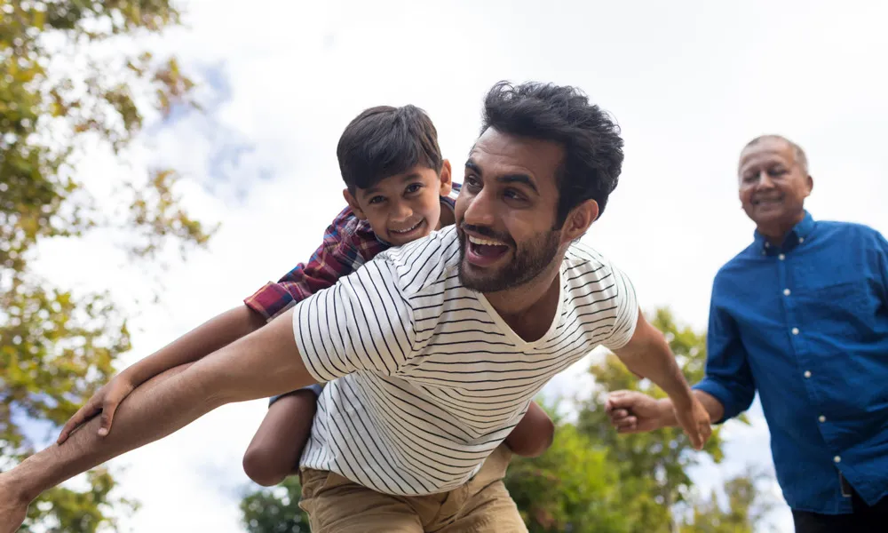man with child on back pretending to fly outside in daytime