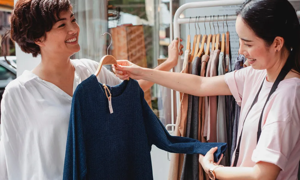 two women looking at clothing on outdoor rack at boutique in daytime