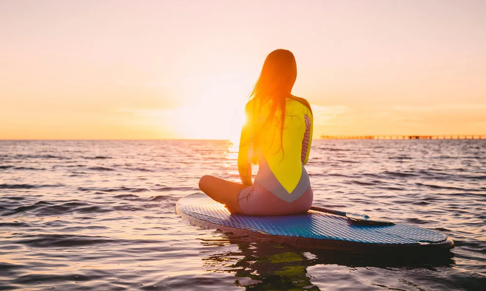 woman sitting on paddleboard in ocean at sunset