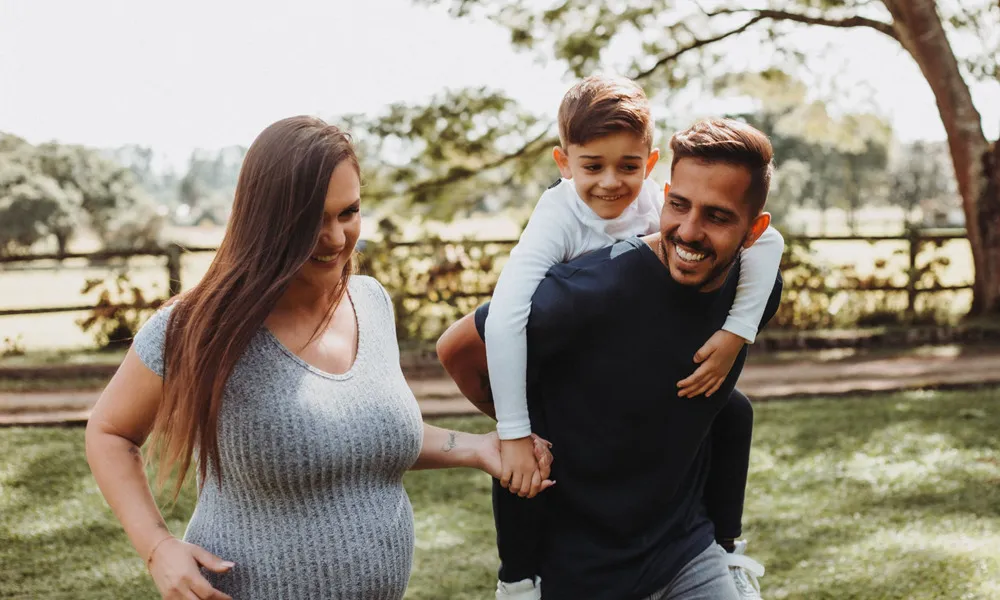 woman holding hands with young boy on man's shoulders in park in daytime