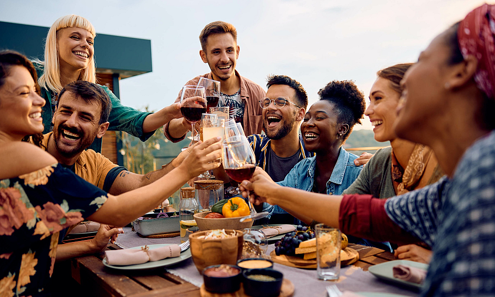 Vibrant group of friends toasting at an outdoor table with food and drinks, enjoying a sunny day.