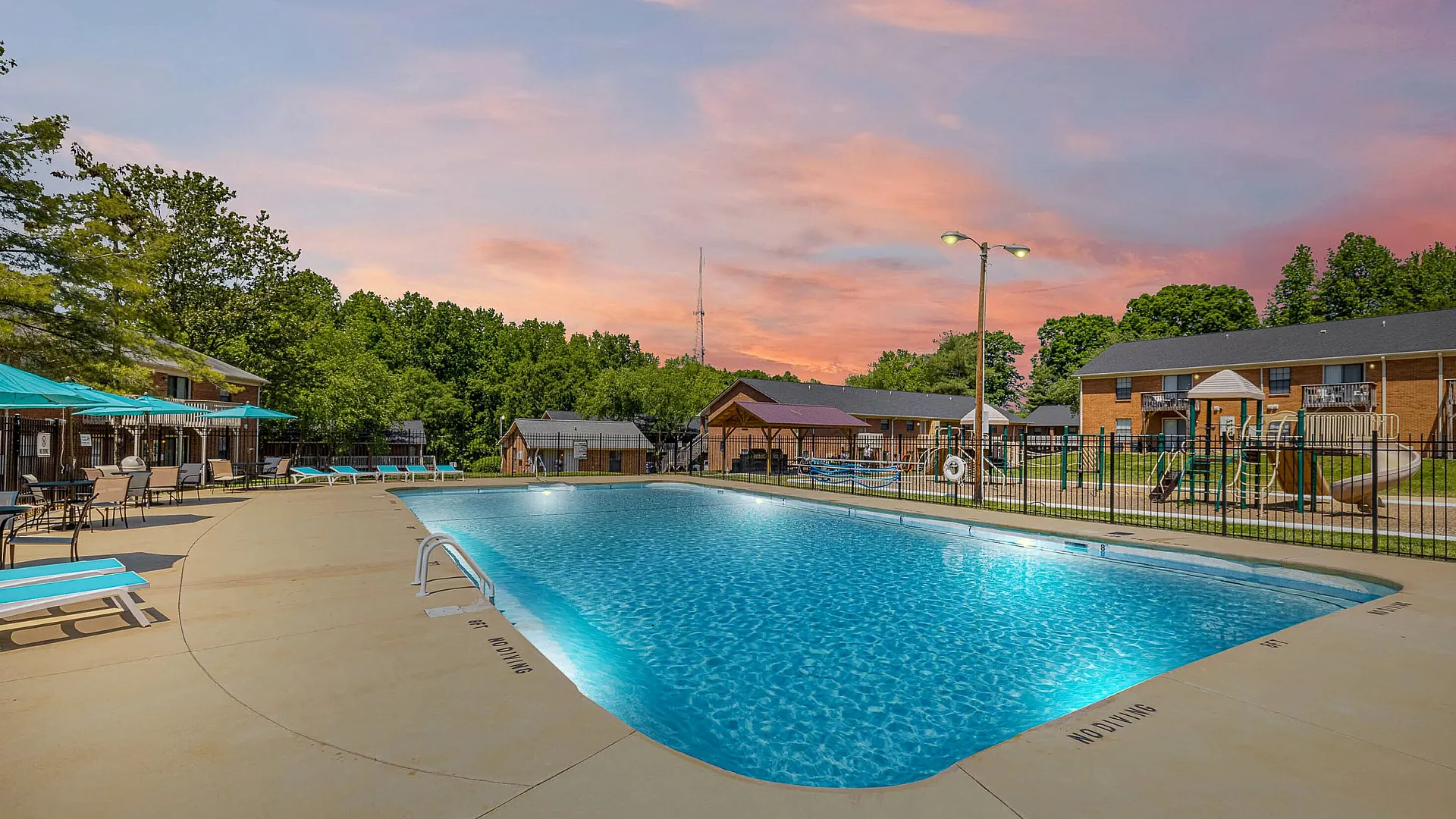 Inviting apartment community pool illuminated at sunset with lounge chairs and trees in the background.