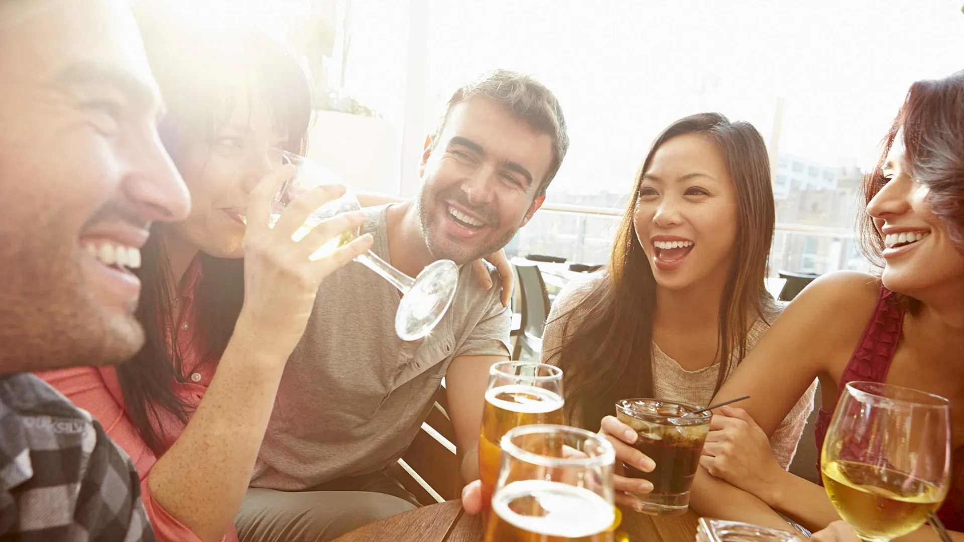 Joyful group of friends enjoying drinks on a sunlit balcony, showcasing a vibrant and welcoming atmosphere.