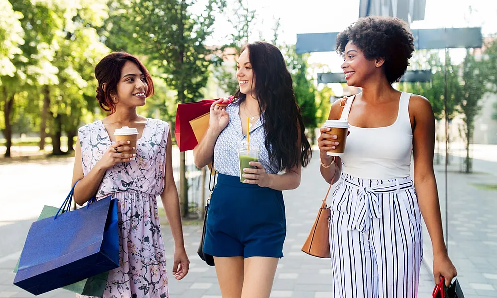 Three joyful women enjoying a day of shopping and drinks in an outdoor urban setting.