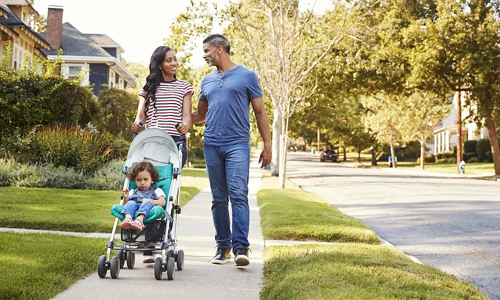 Mom and dad with kid in stroller walking down sidewalk