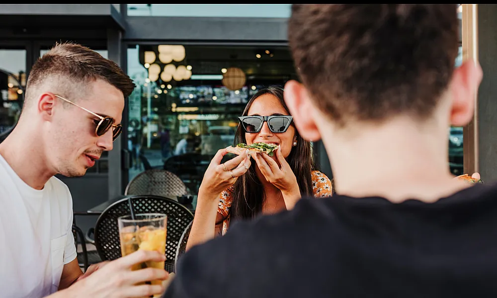 girl eating pizza with two guys at a restaurant