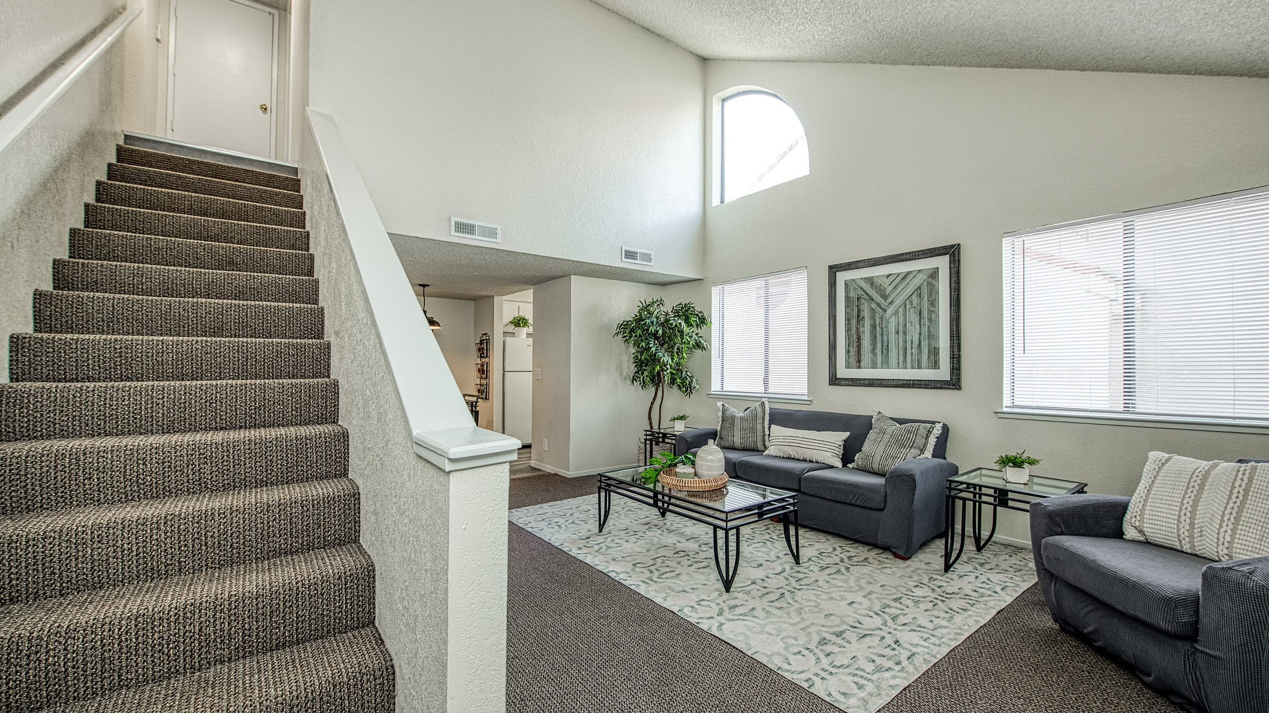Inviting living room with modern gray furniture, elegant decor, and soft natural light, adjacent to a stylish carpeted staircase.