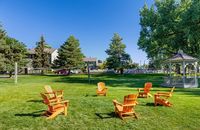 Charming outdoor space with vibrant Adirondack chairs encircling an elegant gazebo, surrounded by lush greenery and mature trees.
