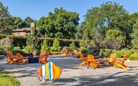 Charming outdoor seating area with vibrant orange chairs and a colorful buffalo sculpture, surrounded by lush greenery and peaceful natural ambiance.
