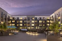 Modern apartment courtyard at Luxor Montgomeryville with lounge chairs, umbrellas, greenery, and a pool, lit under a twilight sky.