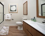Modern apartment bathroom with wood accents, white countertop, glass shower, and decorative wall art.