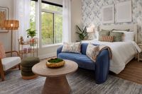 Stylish Montgomeryville apartment bedroom with a blue velvet sofa, wooden coffee table, plush bed, and large windows with greenery.